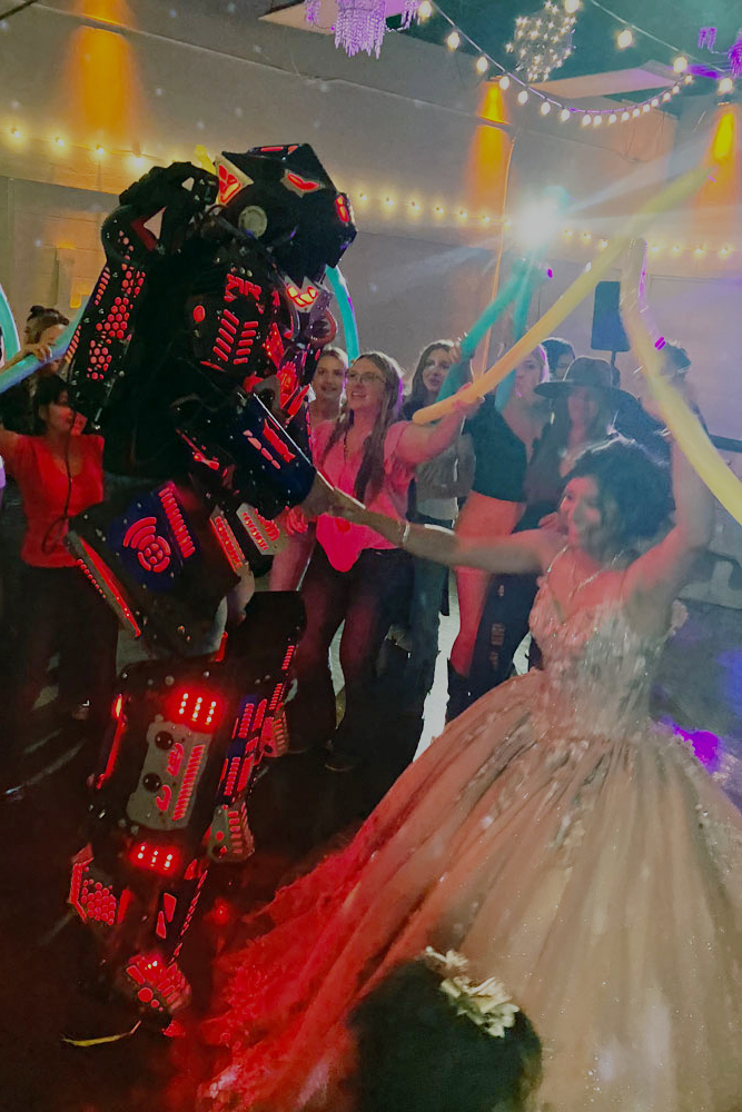 Quinceañera dancing on an illuminated ballroom dance floor with special lighting effects and robot