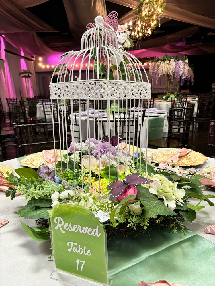 Whimsical bird cage centerpiece design with floral accents, and accent lighting