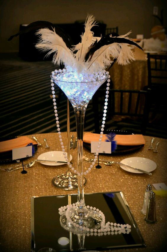 Pearls, ostrich feathers and accent lights on a mirror adorn this guest tables with chargers, dinner ware, and napkins.