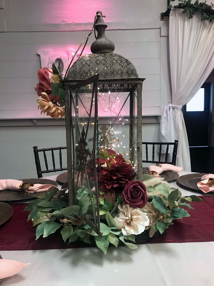 Rustic lantern centerpiece on guest table with chargers and napkins.