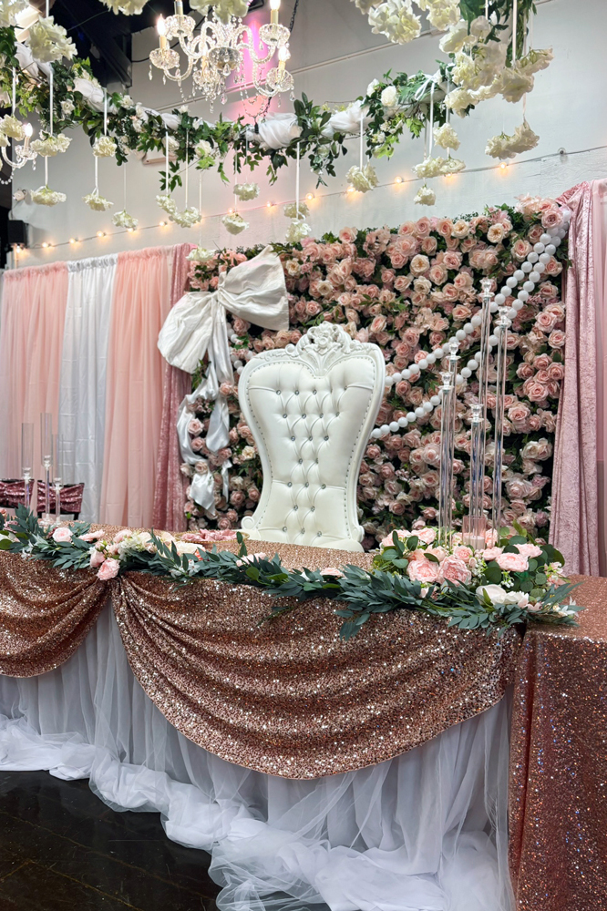 Throne chair at a decorated table of honor in front of a flower wall