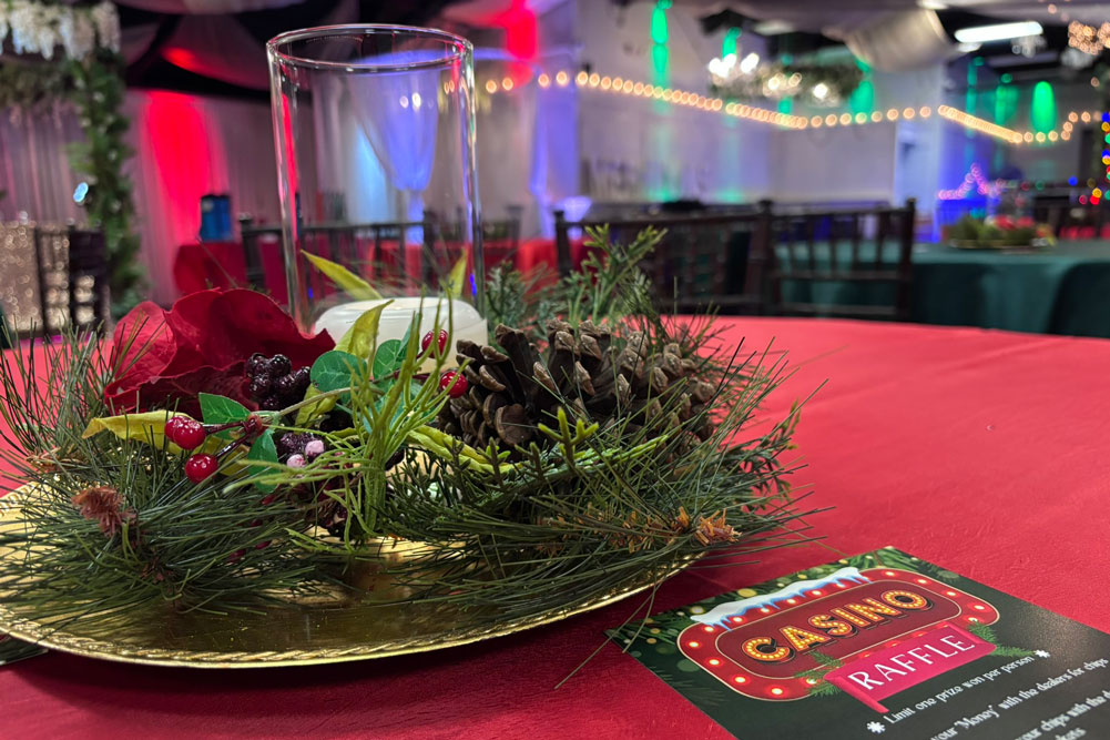 Holiday centerpiece decorated with christmas greenery, a candle, holiday bow, and pine cones.