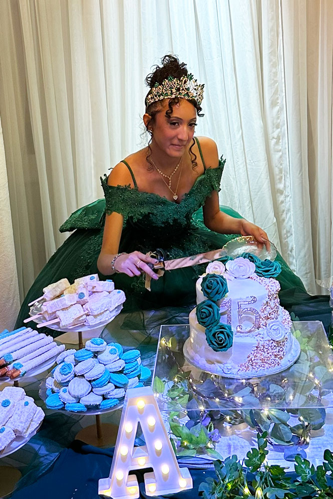 Quinceanera girl cuts cake with cookies, cupcakes, and desserts.