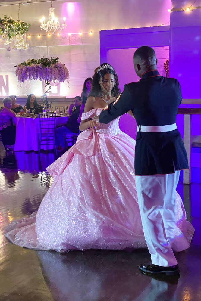 On an illuminated dance floor the quinceaanera girl dances with father.